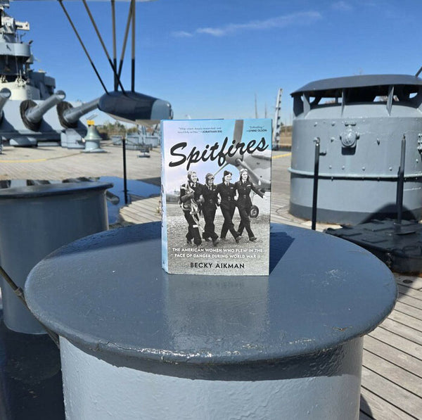 Book titled 'Spitfires' on a naval ship's deck with a clear blue sky.